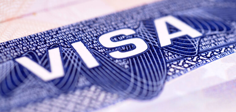 Close-up image of a U.S. visa stamp with the word “VISA” prominently displayed in bold white letters on a blue patterned background.